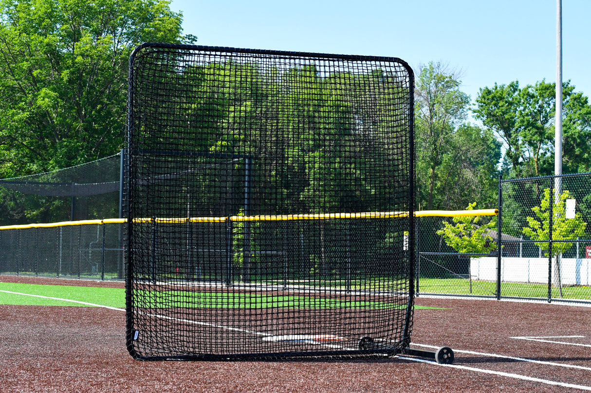 Baseball practice net on a turf baseball field with trees and clear sky in the background